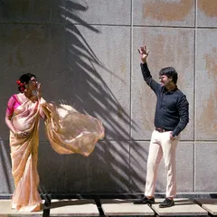 A playful and dynamic maternity shot. The flowing saree and the couple's interaction against the modern, sunlit wall create a feeling of happiness and movement.