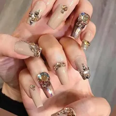 The definition of luxury. These long, square-shaped nails feature a nude base and are heavily adorned with an array of gold and iridescent rhinestones in various shapes and sizes for a truly decadent look.