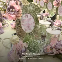 A close-up of a baby girl announcement hamper, featuring a personalized message in a textured silver frame. The arrangement includes baby's breath and soft lavender flowers, creating a delicate and heartfelt welcome gift.