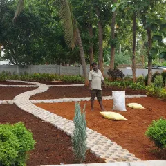 A landscape project in progress. A worker is spreading fresh soil and preparing the ground for planting around a newly laid permeable paver pathway.