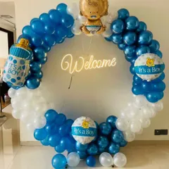 This modern welcome decoration for a baby boy features a full circle balloon arch in blue and white. It includes a "Welcome" neon sign and "It's a Boy" themed foil balloons, creating a perfect spot for family photos.