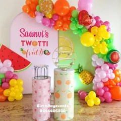 A colorful and juicy "Twotti Frutti" themed second birthday. The decor includes fruit-patterned plinths, a custom backdrop, and a balloon garland with fruit-shaped foil balloons.