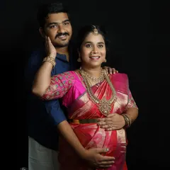 An elegant couple portrait against a simple black background. This style of traditional maternity photography puts all the focus on the couple's connection and the beauty of the silk saree.