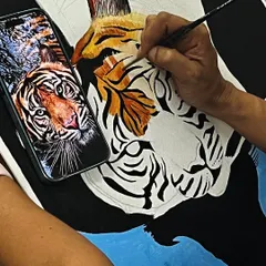 A close up of a student painting a realistic tiger, using a photo reference to capture every detail of the fur and stripes.