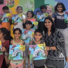 A happy group photo from a four-day acrylic painting workshop. I'm surrounded by my students, all proudly holding up their finished canvases featuring a charming stone bridge over a river.