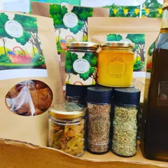 A collection of our organic pantry products. This includes pouches of dried goods, jars of raw honey and spices like cumin and fennel seeds, and bottles of cold-pressed oil.