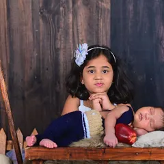 A sweet moment between an older sister and her newborn sibling, who is sleeping in a rustic cart.