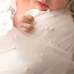 A close up of a tiny hand against a delicate, pearl-studded wrap. This image is all about the contrast in textures and the innocence of a newborn's grasp.