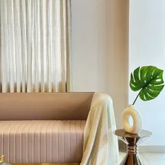 A detail shot of a fluted sofa with a brass base, designed for the Casa Creations showroom. The combination of the soft pink fabric, metallic finish, and the monstera leaf accent creates a look of modern, subtle luxury.