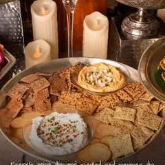A festive platter of French Onion Dip and Roasted Red Pepper Dip with assorted crackers. The warm candlelight and elegant serveware make this perfect for your Diwali party.