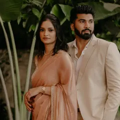 A stylish, editorial-style portrait of the couple, showcasing their coordinated neutral-toned outfits against a lush green backdrop.