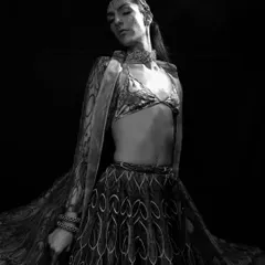 A dramatic black and white image focusing on the flow and pattern of a traditional-style garment. The model's pose and the high-contrast lighting create a powerful, artistic statement.