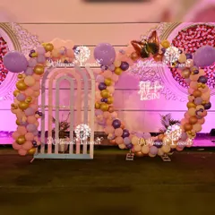 A dreamy butterfly-themed setup for a first birthday party. This design features a large circular balloon arrangement in pastel purple and peach tones, accented with a large butterfly cutout and a "Let the fun begin" sign.