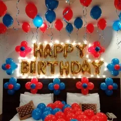 This vibrant birthday decoration uses a striking red and blue color combination. The foil "Happy Birthday" sign is backlit with warm lights, and balloon flowers add a playful touch to the headboard.