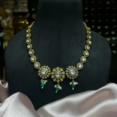 This beautiful Kundan choker features three floral motifs with green drops and pearls. It is a classic design that adds understated sparkle and sophistication to any ethnic outfit.