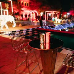 A sleek and modern bar setup for a cocktail night, with high-top tables and chairs set against a backdrop of neon lights and a checkerboard pool. This is where the magic of the night begins.