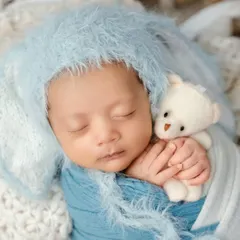 The peaceful, fleeting moments of a newborn are my specialty. I focus on safe and comfortable posing, using soft wraps and textures to create a serene portrait, like this little one dreaming sweetly with his tiny teddy bear.
