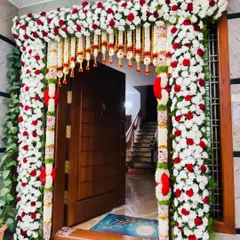 A beautiful floral door decoration for a home, using a thick frame of white chrysanthemums, red roses, and traditional hangings.