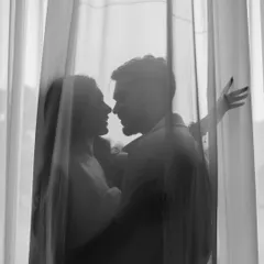 A silhouette of the couple seen through sheer curtains. This intimate black and white portrait focuses on their closeness and the quiet moments shared away from the world.