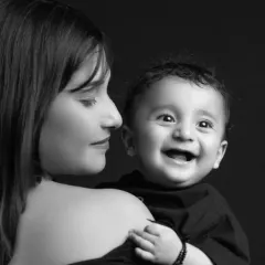 There is nothing more pure than a child's laughter. In this classic black and white studio portrait, the focus is entirely on the joyful connection between mother and baby. The dramatic lighting isolates their expressions, creating a powerful and timeless memory of a fleeting moment.