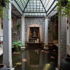 The stunning indoor pond in our Heritage Villa, with a glass ceiling, stone pillars, and a serene Buddha statue, creating a tranquil oasis.