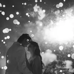 A magical sangeet moment captured in timeless black and white. The silhouette against the fireworks creates a dreamy, star-struck atmosphere, freezing a fleeting second of pure celebration and romance into an unforgettable memory.