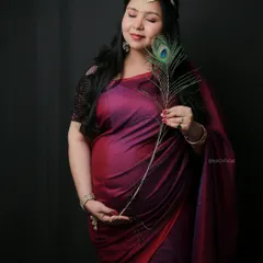 A graceful solo portrait in a rich magenta saree, using a peacock feather as an elegant prop.