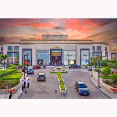 A wide daytime shot of the DLF Emporio entrance, capturing the flow of traffic and people. The dramatic sky adds a dynamic quality to this architectural photograph.