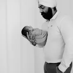 A full-length black and white portrait of the father standing while holding his tiny newborn. This composition emphasizes how small and precious the baby is.