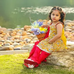 This little girl in a traditional outfit sits gracefully on a rock by the water, holding a basket of flowers. Outdoor settings provide a beautiful and natural backdrop for portraits.