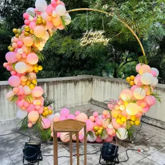 This circular ring backdrop is a popular choice for modern celebrations. Here, I've decorated it with a vibrant mix of pink, peach, and gold balloons and a "Happy Birthday" neon sign for a chic outdoor party on a terrace.