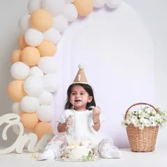 Messy hands and a happy face. This little girl is having the best time at her elegant cake smash, set against a beautiful arch of balloons.