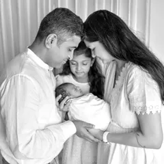 A beautiful black and white portrait of a family of four welcoming their newest member. The image focuses on the tender moment as they all gaze lovingly at the newborn.