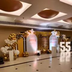This is a wide view of a grand 55th birthday celebration I designed. The setup includes a large gold sequin backdrop, custom arched panels, '55' marquee numbers, and extensive balloon garlands in a white and gold theme.