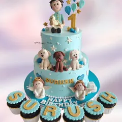 A truly personalized two-tier cake for a 1st birthday celebration. This design features the birthday boy with his beloved pets, angels, and matching cupcakes that spell out his name.