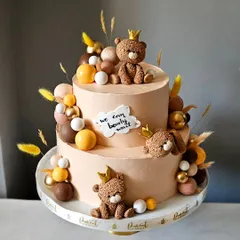 A chic and modern baby shower cake in a bohemian theme. This two-tiered cake features earthy tones, dried grasses, and adorable, hand-sculpted teddy bears wearing little crowns.