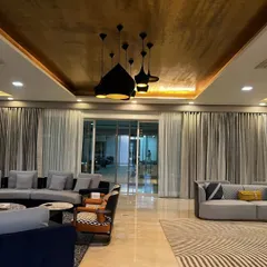 The living room at our Vasant Kunj farmhouse project features a dramatic gold-textured ceiling and modern black pendant lights. The design combines sleek, contemporary furniture with bold patterns, creating a sophisticated and inviting atmosphere for a large family.