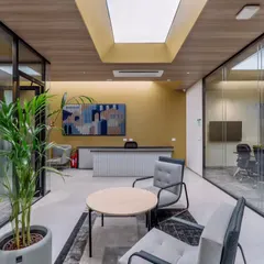 The reception area of the RATNAAFIN office sets a modern, professional tone. A central skylight brings in natural light, illuminating the clean lines, wood-paneled ceiling, and comfortable seating that welcomes visitors and employees.