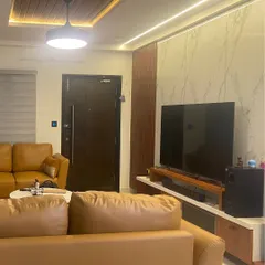 This living room combines comfort with smart technology. The television area is complemented by automated ceiling and accent lighting, all controlled via discreet wall panels and a central app for a seamless entertainment experience.