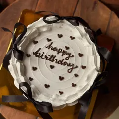 A Pinterest-inspired birthday cake with a clean white finish, delicate chocolate hearts, and chic black ribbon bows.