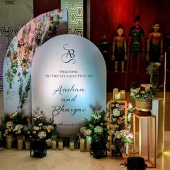 A modern arched welcome sign for Aashna and Bhargav, featuring their custom monogram. The sign is surrounded by soft florals and candlelight, creating a romantic and personalized entryway.
