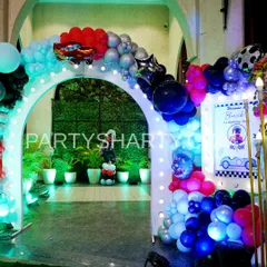 An illuminated entrance arch for a car party, decorated with balloons and a Lightning McQueen foil balloon, leading to a lush green backdrop.