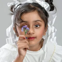 Capturing the innocence and wonder of childhood in a creative portrait. This studio shot for a child's portfolio uses soft lighting and simple props like the flower and ribbons to create a sweet, artistic image that feels both timeless and full of personality.