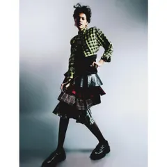 A full-length studio portrait from 'My Flatmate's Wardrobe,' featuring an eclectic, layered plaid outfit. The clean background and dynamic pose highlight the unique personal style celebrated in this series.
