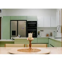 A modern, functional kitchen with pastel green ribbed cabinetry and integrated appliances. The design combines sleek white upper cabinets for a light feel with an L-shaped counter that doubles as a breakfast bar.