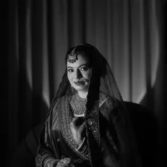 A classic black and white bridal portrait. The dramatic spotlight effect creates a vintage, cinematic feel, highlighting the bride's grace and beauty in a timeless way.