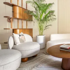 A sculptural wooden partition subtly divides the space, adding an artistic element while maintaining the open and airy feel. A large plant brings a touch of nature indoors, enhancing the room's tranquil vibe.