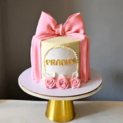 A classic and beautiful bow cake. This design features a perfectly draped pink fondant bow over a white ganache cake, accented with a pearl border and delicate sugar roses.