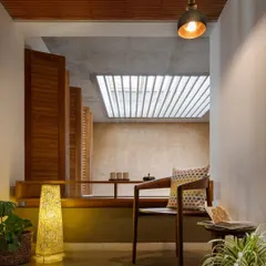 This quiet nook overlooking an internal courtyard is the perfect spot for a morning cup of tea. The design uses natural materials like wood and a mud-finished wall to create a warm, tactile, and calming atmosphere.