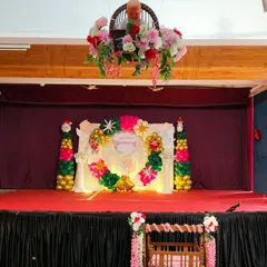 A wide view of the stage decorated for 'Blossom's Christening'. The setup includes the main backdrop, a decorated cradle in the front, and a floral arrangement hanging from the ceiling.